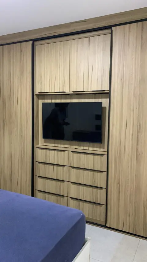 Quarto com painel de TV amadeirado, gaveteiro e armário superior